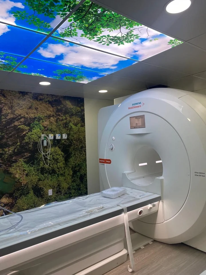 Sala de ressonância magnética com forro ilustrado com céu e árvores.
